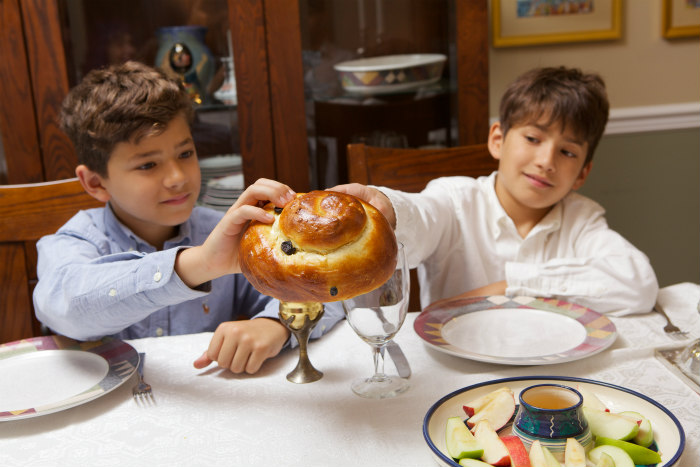 Two young boys holding a round challah with a platter of apples and honey in front of them