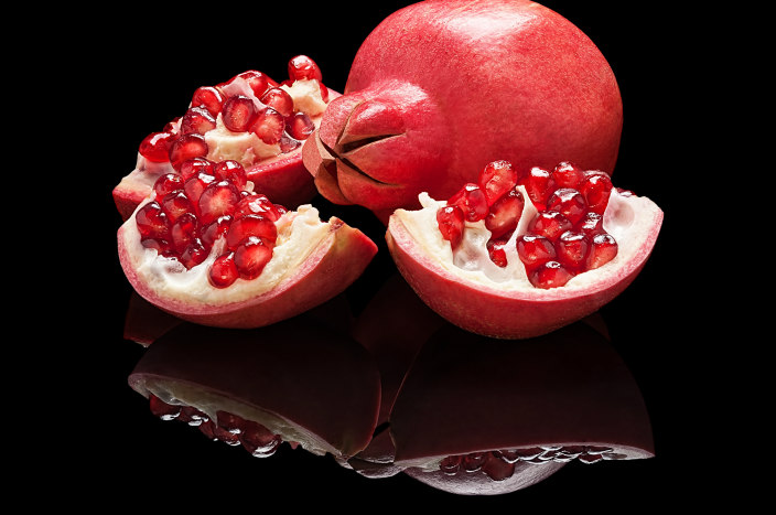 Two pomegranates sitting on a black reflective surface with their mirror images shown below 