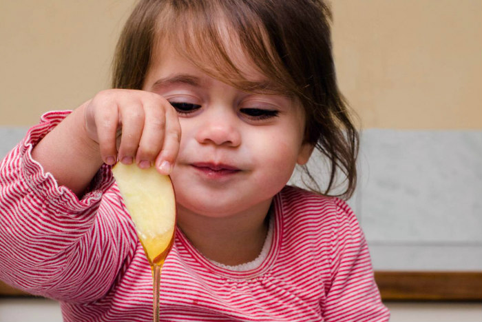 Young girl dipping an apple into honey