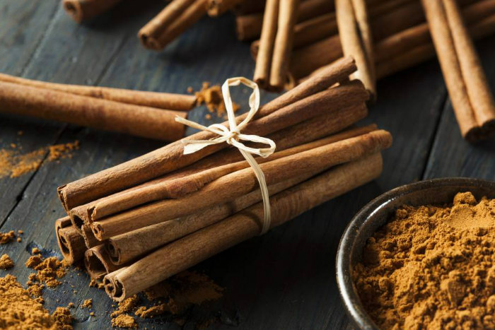 Bundle of cinnamon sticks tied with a ribbon next to a small bowl of ground cinnamon