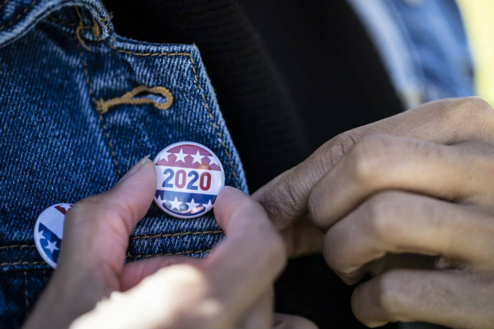 Closeup of a hand affixing a red white and blue 2020 button to a denim jacket