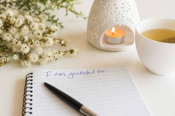 Desktop setting with a small candle and some flowers along with a pad of paper reading I AM GRATEFUL FOR