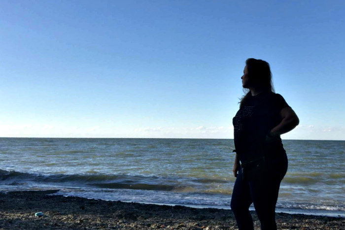 Silhouette of a woman with her hand on her hip staring out over a body of water