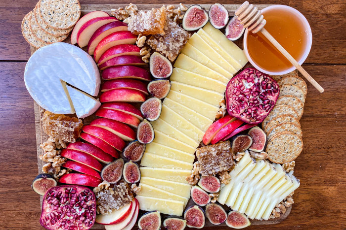 Decorative Rosh HaShanah cheese board featuring cheese apples honey crackers and walnuts