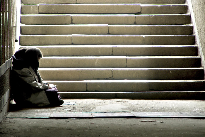 Bundled up homeless person in the shadows at the bottom of a cement stairwell