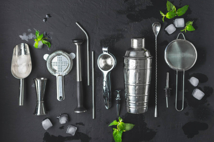 Bar tools like a shaker and strainer against a grey background 