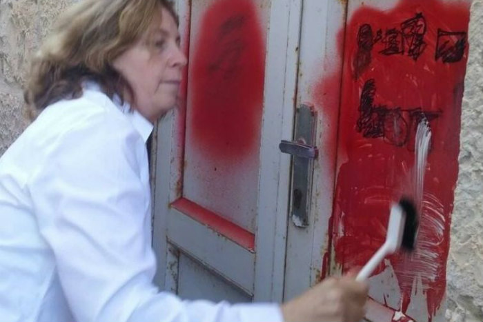Anat Hoffman scrubs graffiti off of a cement wall