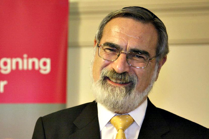 Smiling image of Rabbi Jonathan Sacks wearing a black jacket with a yellow tie 