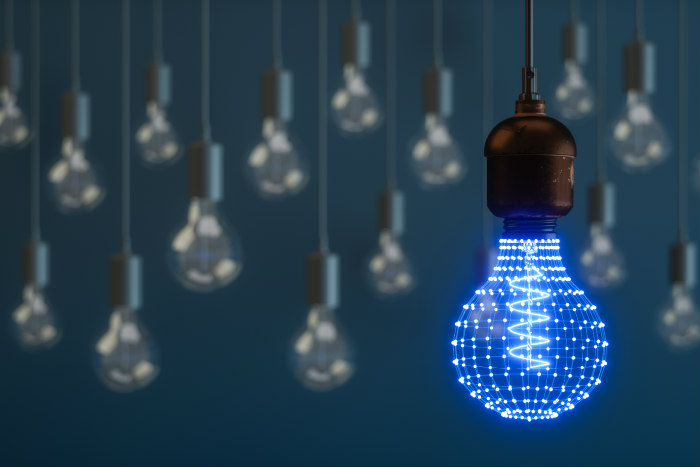 Lightbulbs hanging from a ceiling with one in the front glowing blue 