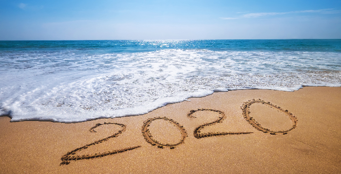 Beach with 2020 written in the sand and a wave coming to wipe it out