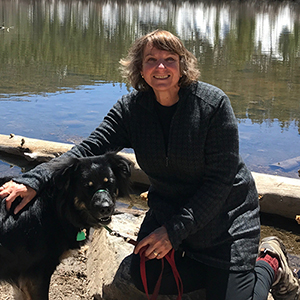 Marilyn Shapiro poses in front of a body of water with a black dog 