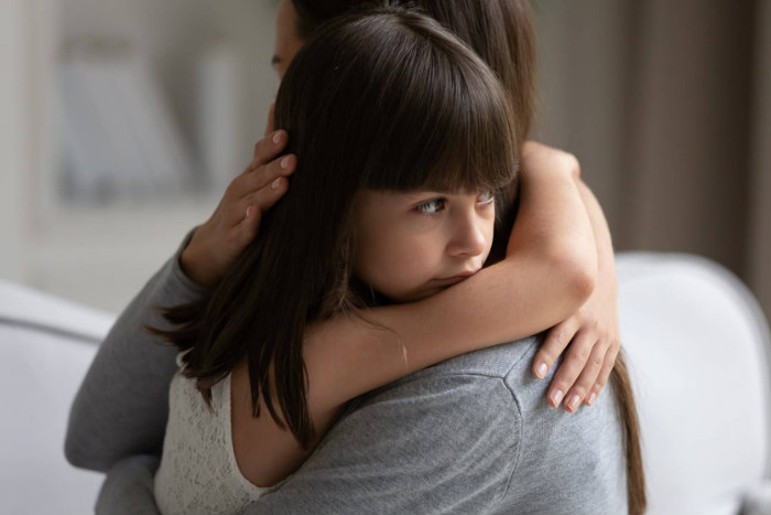 Young girl looking sad as she is hugged by an adult woman