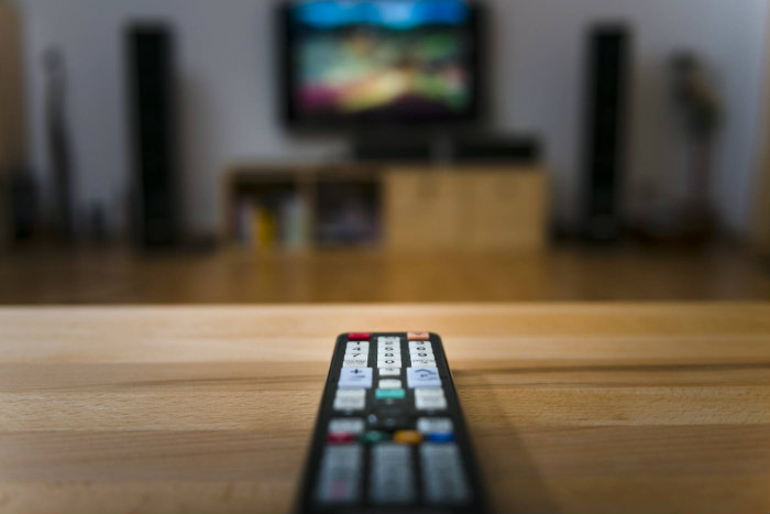 A remote control pointed at a blurry TV in the background