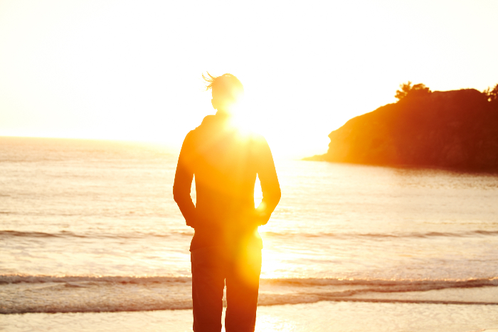 Silhouette of an unidentifiable person standing on a beach at sunset obscured by a sunbeam