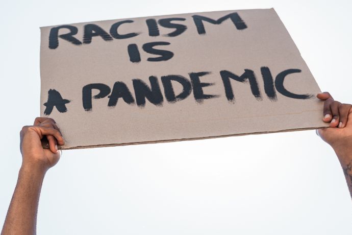 Hands holding up a cardboard sign that reads RACISM IS A PANDEMIC