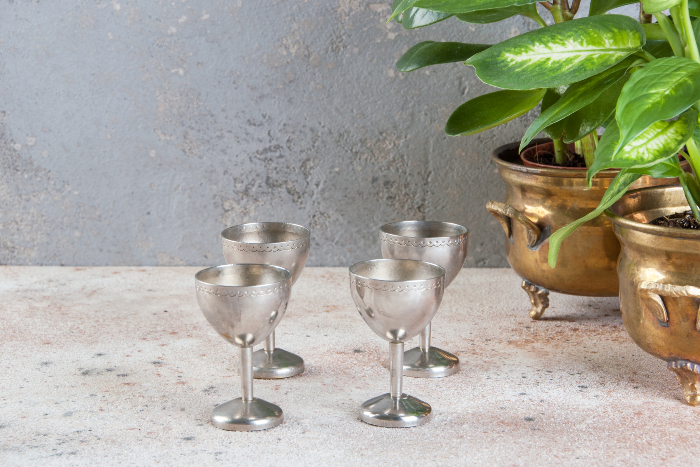 Four vintage silver wine glasses next to a plant