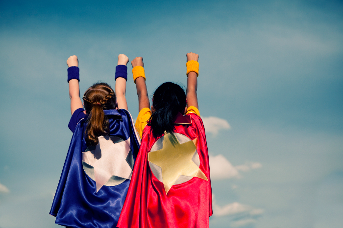 Two young girls facing forward wearing superhero capes 