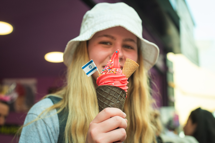 Teenage girl holding an ice cream cone to the camera with a tiny Israeli flag stuck in it 