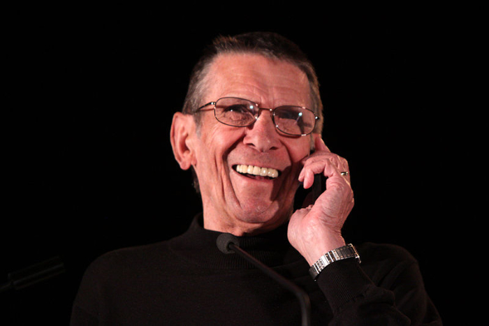 Image of a laughing Leonard Nimoy with his hand on his chin against a black background