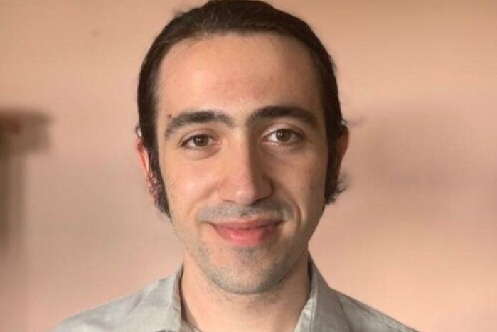 Headshot of Aaron Bendich with his hair pulled back in a ponytail against a pink background