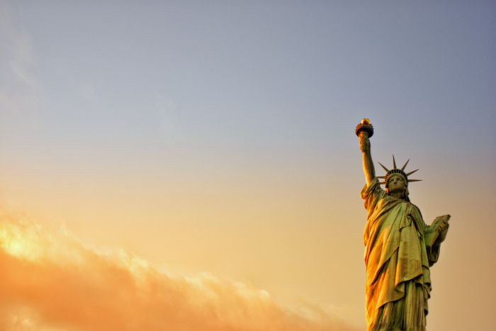 Statue of liberty lit against an orange and yellow sunset