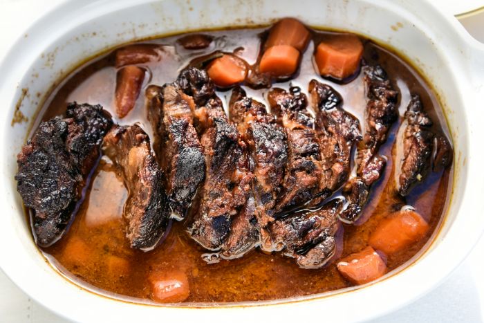 Closeup of brisket surrounded by roasted carrots in a white pan 