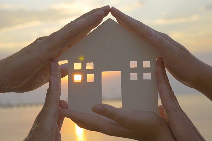 an image of four hands in the shape of a house with an image of a small house inside of them and water in the background