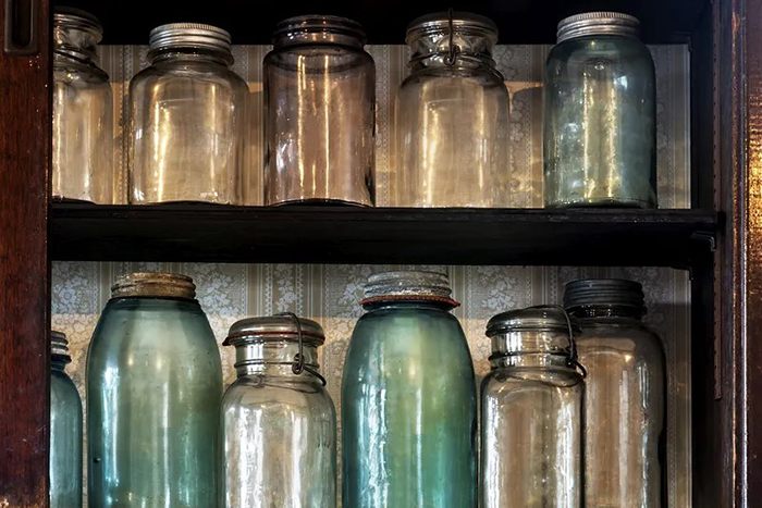 an image of different types and colors of jars sitting on two shelves in a cabinet