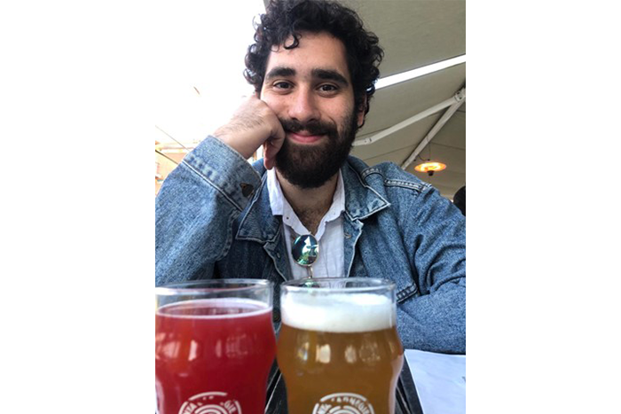 A person in a blue jean jacket sitting at a table in front of two glasses of beer