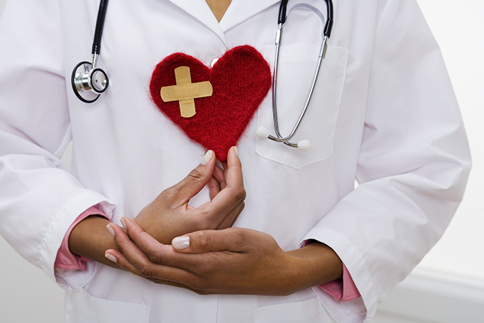 an image of the body of a femail doctor wearing a doctor oat and holding a red heart with two bandaids in the shape of a cross on it