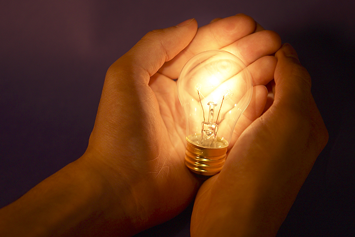 an image of two hands holding a lit up light bulb
