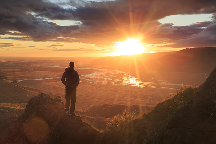an image of a man standing on top of a mountain with the sun setting in the background
