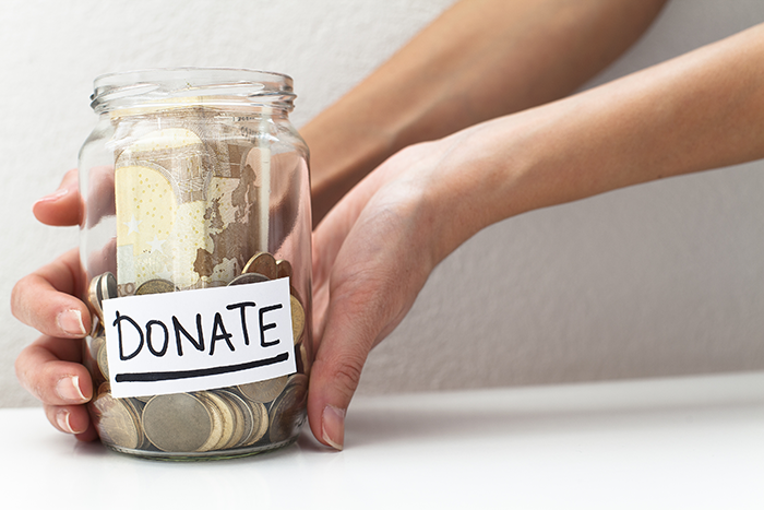 an image of two hands holding a jar full of money that says "Donate" in black ink on a white sticker