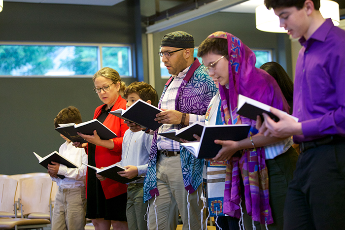 Photo of six people, adults and children, holding and looking down at a prayer book