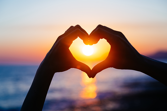Photo of two hands, making a heart shape, with the sun appearing through it