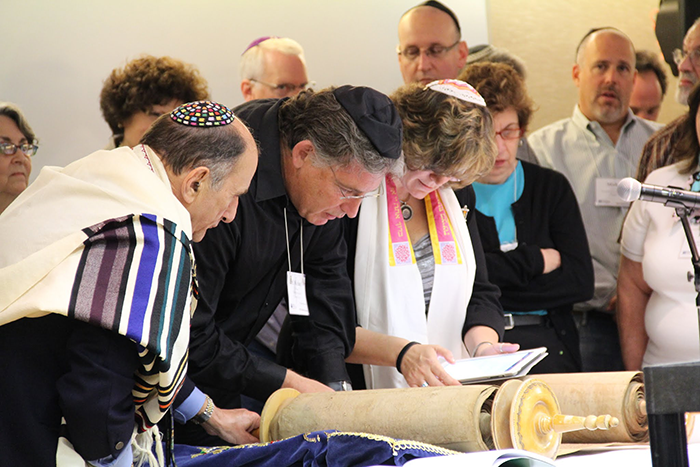 A photo of two men and a woman looking down at a Torah scroll