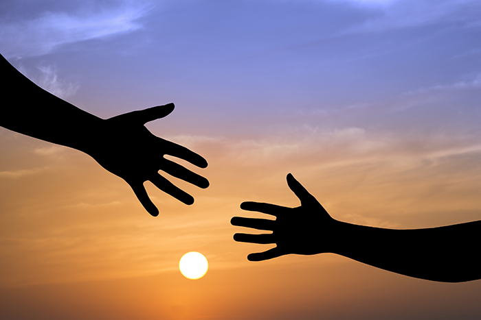 Photo of the silhouette of two hands reaching for each other in front of a sun set