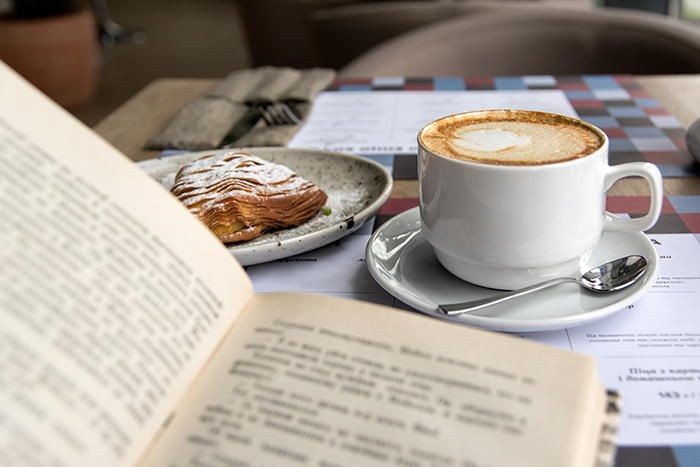 Photo of a book with a cup of coffee and a pastry sitting on a table
