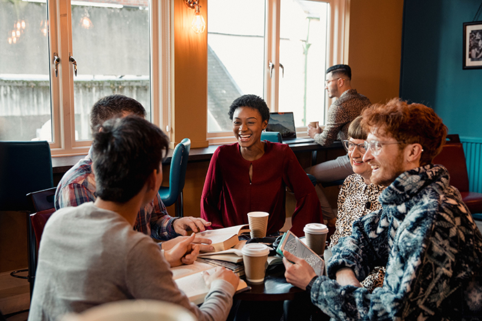 Photo of a group of people of different genders and nationality sitting around a table and talking