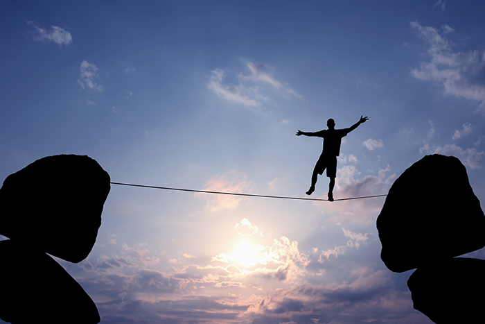 Photo of a person walking on a tightrope between two big rocks
