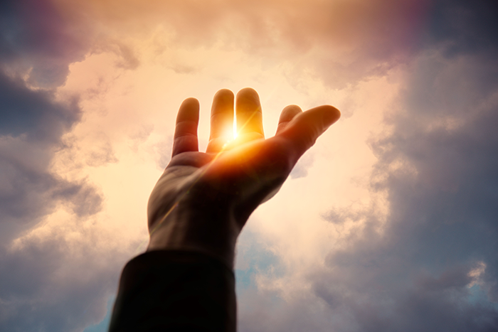 Photo of a hand reaching up with the sun shining from behind the hand