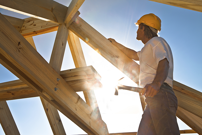 Photo of a man building a house; using a hammer to nail two studs together