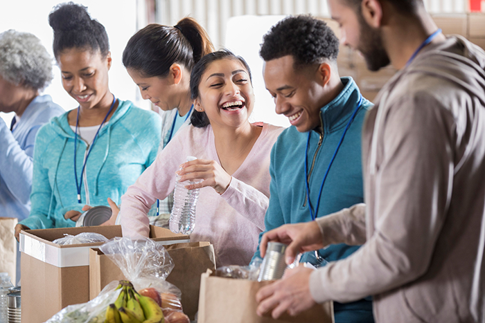 Photo of a group of people talking while volunteering by packing grocery bags and boxes full of fruit, water bottles and canned goods.