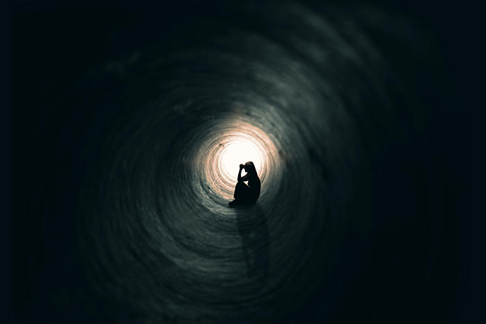 Photo of a worried person sitting in a dark tunnel