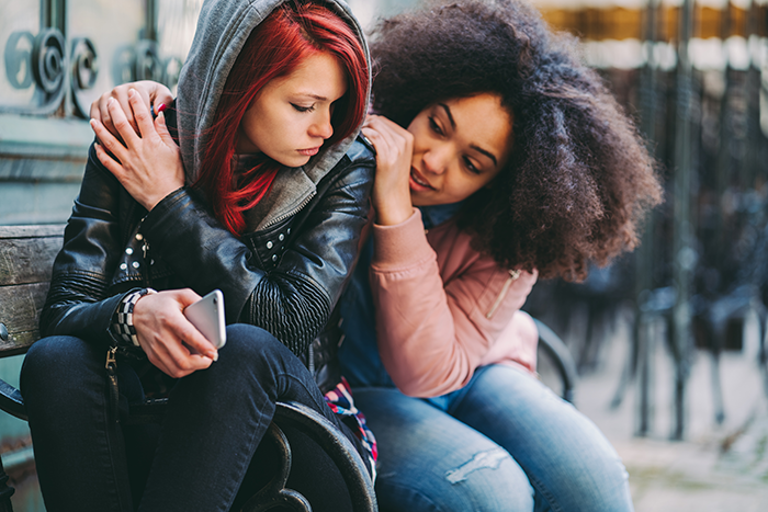 Photo of two girls, one hugging another who looks depressed