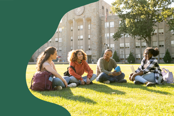 Photo of four college students sitting on the grass outside a building