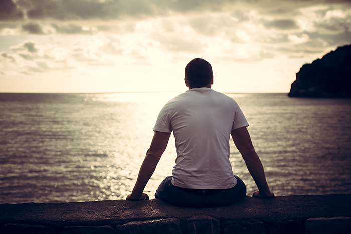 Photo of a man sitting by himself looking at a lake