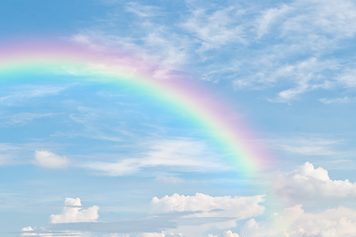 Photo of a rainbow in a bright blue, cloudy sky