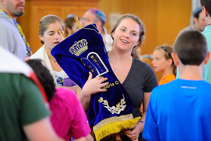 Photo of a teenage girl holding a Torah and walking about the room
