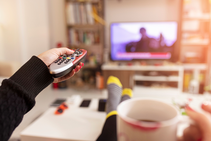 Photo of a person's arm, holding a remote control, pointing it towards a tv set that's on